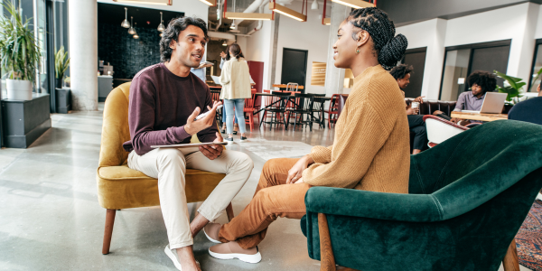A man and a women in an office setting sitting on chairs and talking